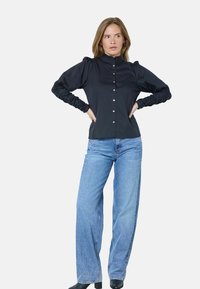 Zwarte blouse met opbollende mouwen en geplooide manchetten, gecombineerd met lichtblauwe wijde jeans en zwarte enkellaarsjes. Eenvoudig ontwerp, gladde textuur.