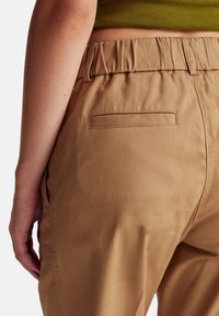 Světle hnědé kalhoty s volným střihem, vybavené elastickým pasem, postranními kapsami a jednou zadní kapsou pro detaily. Měkká struktura tkaniny.