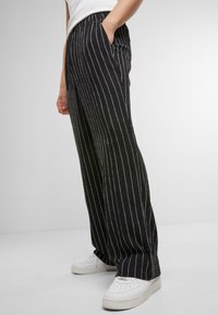 Pantaloni largi cu dungi negre, dintr-un material texturat, având talie înaltă și buzunare laterale, asortați cu adidași albi.