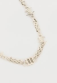 Ασημένιο κολιέ αλυσίδα με αλληλοπεμπλεγμένους κρίκους, που διαθέτει ένα στυλιζαρισμένο μενταγιόν "B" και διακοσμητικά εμπνευσμένα από συρματοπλέγματα.