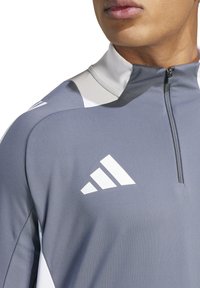 Maglione atletico grigio a mezza zip con accenti bianchi e logo in rilievo, realizzato in materiale liscio ed elastico con un design aderente.