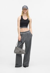 Μαύρο crop top με λογοτύπο, γκρι χαλαρές παντελόνες και γκρι υφασμάτινη τριγωνική τσάντα με λογότυπο. Το καπέλο είναι επίσης γκρι και έχει έναν παpatch.