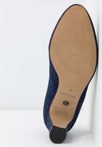 Escarpin en daim bleu marine avec semelle lisse couleur tan, motif de grip texturé près des orteils et talon bas en caoutchouc noir.