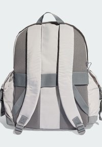 Svetlosivý batoh s sieťovaným zadným panelom, polstrovanými popruhmi a bočnými vreckami. Má nastaviteľné popruhy a logo na kovaniach.