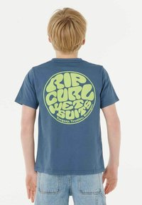 T-shirt en coton bleu à manches courtes avec un grand texte arrondi jaune-vert au dos, indiquant "RIP CURL WET SUITS" avec des détails de localisation.