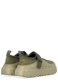 Coppia di scarpe slip-on verde oliva con suole spesse beige, tomaia in camoscio e tessuto, e cinturino regolabile in velcro con logo UGG.