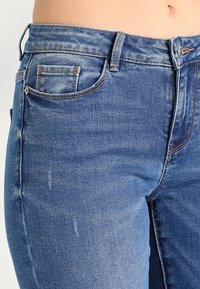 Tummansinisiä farkkuja, joissa on haalistunut pesu, viiden taskun muotoilu, vyölenkit ja näkyvät ompeluyksityiskohdat.