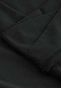 Tissu noir avec coutures visibles et plis, mettant en valeur la texture lisse et les détails des coutures en gros plan.