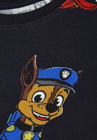 Sudadera negra con un perro de dibujos animados que lleva una gorra de policía azul, una placa de estrella amarilla y detalles faciales brillantes, diseño de tela texturizada.