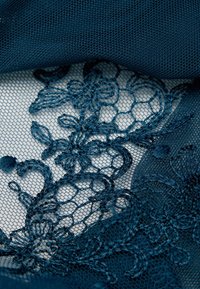 Tissu en dentelle bleu foncé avec broderie florale sur un fond de maille fine, mettant en valeur des motifs complexes et des accents texturés.