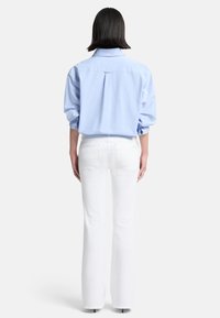 Camicia button-up azzurro chiaro con maniche lunghe, abbinata a jeans bianchi a campana. La camicia presenta una piega sul retro e un colletto classico.