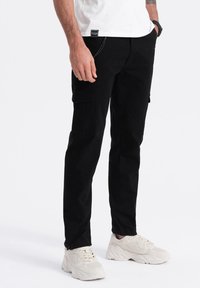 Černé cargo kalhoty s několika kapsami, slim fit, vyrobené z pevné látky. Mají detailní švy a zipy na kotnících.