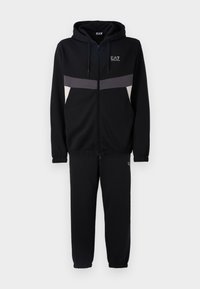 Black sweatshirt and joggers set, featuring a zip-up hoodie, gray and white stripe accents, made from soft, textured fabric. EA7 logo displayed.