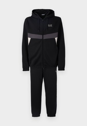 Completo di felpa nera con zip e pantaloni jogger, caratterizzato da dettagli a strisce grigie e bianche, realizzato in morbido tessuto testurizzato. Logo EA7 visibile.