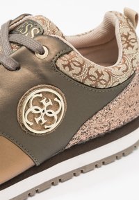 Der Schuh besteht aus einer Kombination von olivgrünen und beigen Materialien, strukturiertem Stoff, einem goldenen Logohighlight und einer weißen Außensohle mit Profil.