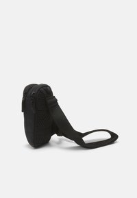 Černá crossbody taška s texturovanou síťovinou na boku, zipovými kapsami a nastavitelným popruhem. Kompaktní tvar, hladký materiál a jednoduchý design.