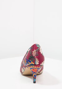 Scarpa con tacco alto color bordeaux decorata con vivaci ricami floreali in blu, verde e oro. Tessuto in raso con punta affusolata e design del tacco sottile.