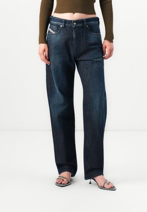 Person wearing dark blue straight-leg jeans, brown long-sleeve cropped top, and open-toe high-heeled sandals with thin straps.