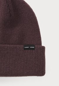 Dark purple knit beanie with ribbed texture, featuring a folded cuff and a small black label with white text at the side.