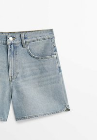 Krótkie spodenki dżinsowe wykonane z jasnoniebieskiej bawełny, z klasycznym pięciokieszeniowym krojem, zapinane na guzik, z podszytymi brzegami z delikatnym postrzępieniem.