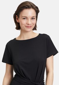 Abito t-shirt nero con scollatura rotonda e maniche corte. Il tessuto è liscio, con un dettaglio annodato in vita per un look aderente.