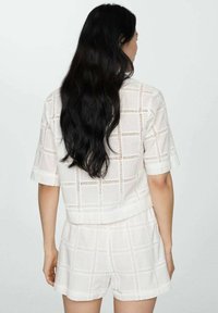 Witte cropped top en shortset, gemaakt van textuurstof met een opengewerkt rasterpatroon. Korte mouwen en een relaxte pasvorm, lichtgewicht materiaal.