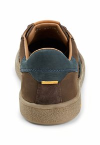 Brun ruskind på bagsiden af en sneakers med en mørkeblå detalje og gule hardwarekomponenter. Tekstureret sål med beige finish. Indvendigt har den en tan-farvet foring.