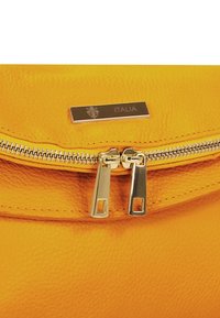 Gelbe Lederhandtasche mit Reißverschluss, zwei silberfarbenen Reißverschlussgriffen und einer goldfarbenen Plakette mit der Aufschrift "ITALIA".