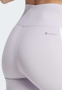 Grijze leggings met een hoge tailleband, gemaakt van een glad, rekbaar materiaal. Heeft een klein "AEROREADY" logo nabij de tailleband.