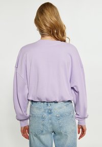 Oversized bluza z lawendy o prążkowanej fakturze i opadającymi ramionami, zestawiona z jasnoniebieskimi spodniami z wysokim stanem, które mają tylne kieszenie.