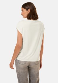 T-shirt à manches courtes en crème clair, col rond, tissu doux, coupe ample, associé à un pantalon gris clair avec poches arrière.