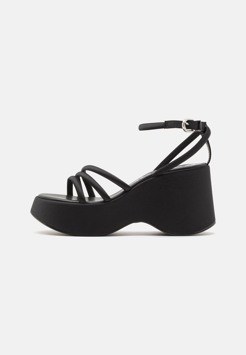 Black platform sandals with multiple thin straps and a buckled ankle strap. Features a wide, curved sole for support and stability.