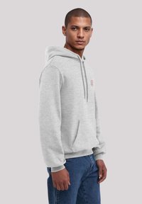 Grauer Baumwollhoodie mit einer Vordertasche, verstellbarem Kordelzug und gerippten Bündchen. Hat ein kleines rotes Logo auf der linken Seite.