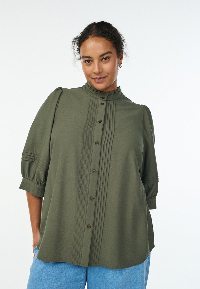 Olivgrön skjorta med hög krage, knappfront och plisserade detaljer. Har puffärmar med subtila randiga accenter. Mjuk, texturerad tyg.