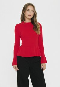 Top a coste rosso con maniche lunghe a campana e orlo peplum, abbinato a pantaloni neri. Tessuto liscio e design aderente.