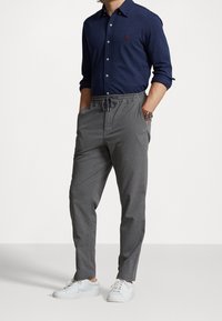 Marinblå skjorta med knäppning och långa ärmar samt grå dragsko-byxor; vita sneakers fulländar outfiten. Har polo-logotyp på bröstet.