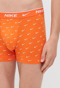 Narancssárga pamut boxeralsó, fehér Nike swoosh mintázattal, és illeszkedő gumírozott derékpánttal, amelyen a Nike logó található.
