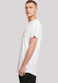 White cotton t-shirt with short sleeves, featuring multicolored text "PRINCESS" and "DANIEL" across the chest. Relaxed fit, side slit detail.