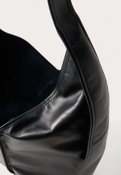Μαύρη λείο δερμάτινο τσάντα ώμου με φαρδιά τιράντα και ορατά ράμματα, εμφανίζεται σε κοντινή λήψη μπροστά σε ανοιχτό φόντο.