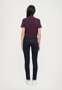 Sötét farmer skinny farmernadrág rövid ujjú bordó inggel és fehér tornacipővel párosítva. Kiemelkedő varrásokkal és hátsó zseb kialakítással rendelkezik.
