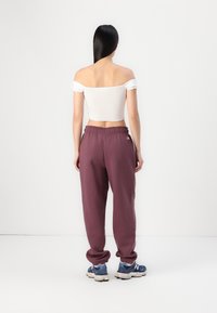 Bijela crop majica bez naramenica i bordo trenirke s elastičnom gumom u struku, uparene s plavim tenisicama koje imaju bijeli detalj s logotinom.