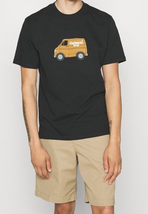 Camiseta negra con gráfico de furgoneta vintage naranja y texto "Carhartt WIP" usada con pantalones cortos beige en una persona con tatuajes en los brazos.