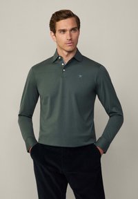 Polo tričko s dlouhým rukávem ve tmavě zelené bavlněné směsi, s límečkem, knoflíkovou légou a jemným logem na hrudi. Texturovaný vzhled.