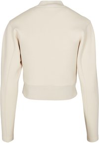 Ulltröja i ljusbeige med långa ärmar. Slät textur och ribbad nederkant samt krage. Enkel design utan synliga knäppningar eller mönster.