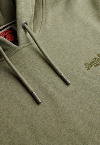 Oliven grøn hoodie lavet af blødt, tekstureret stof. Har en hætte med snoretræk, metal detaljer på snorene og broderet logo på forsiden.
