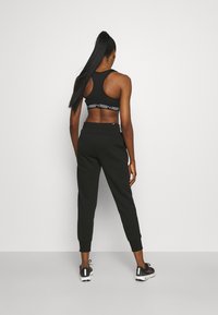 Sostenedor deportivo negro de diseño tipo racerback con banda con logo, combinado con pantalones jogger negros que tienen puños elásticos y sutiles bolsillos laterales.