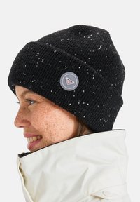 Zwarte gebreide beanie met witte spikkels, voorzien van een ronde logo-tag. De textuur is geribbeld en het ziet er warm en snugger uit.