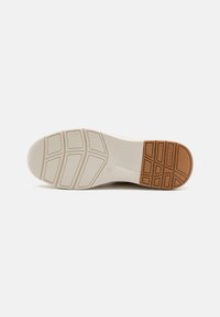 Semelle en caoutchouc blanche avec une surface texturée, comportant une section en caoutchouc beige au talon et des rainures définies pour l'adhérence.