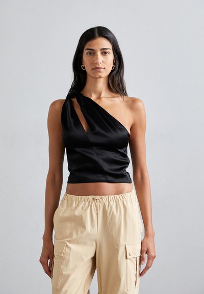 Schwarzes satin asymmetrisches Top mit einem einzelnen Schulterträger und einem Schlitz vorne, kombiniert mit locker sitzenden, hellbeigen Cargo-Hosen.