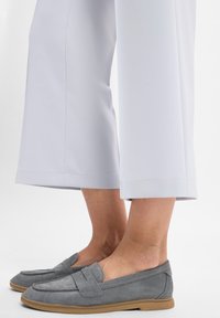 Grijze suède instappers met een lage profiel, met een gestikt bovenband en een rubberen zool, gecombineerd met lichtgrijze cropped broek.